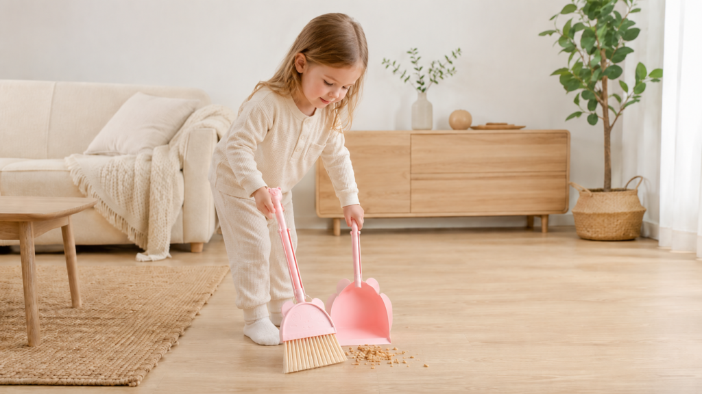 White child using a pink kids broom and dustpan set for Montessori-inspired home cleaning practice